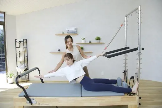 リフォーマーでレッスンを受ける女性とトレーナー