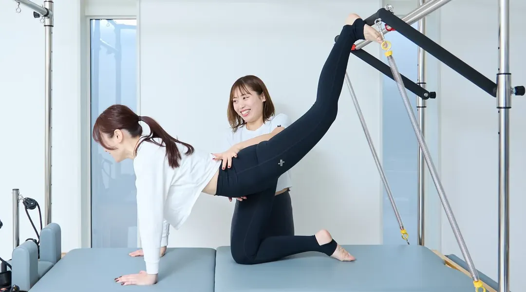 キャデラックでトレーナーに支えられながら脚を伸ばす女性（引き締め・ボディメイク）