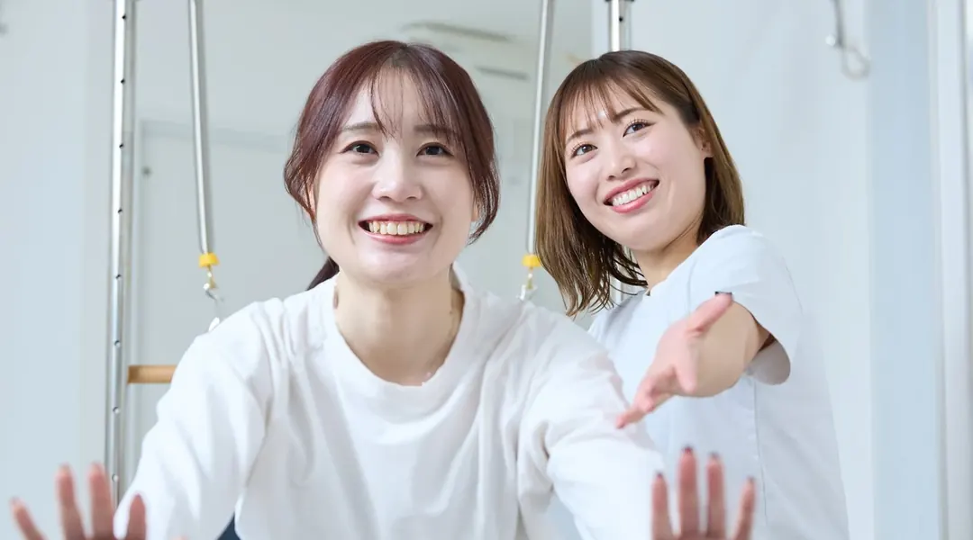 笑顔でトレーナーに教わりながらレッスンを受ける女性（自律神経の改善）