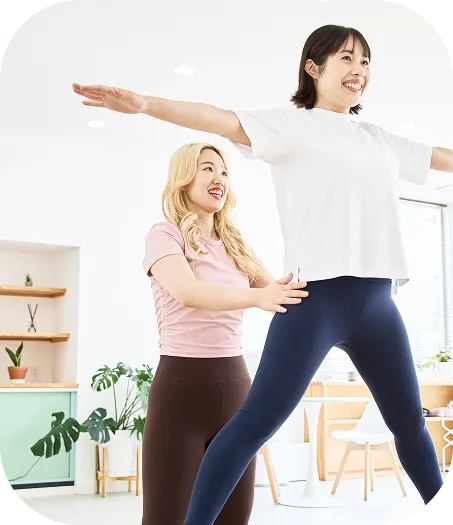 トレーナーと一緒にピラティスのエクササイズを行う女性