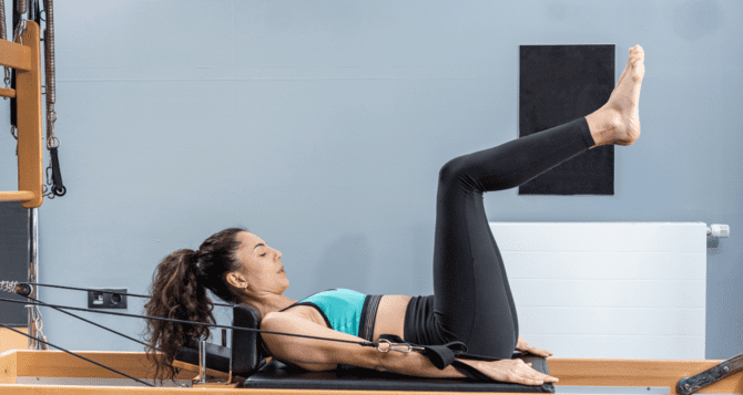 Woman in bra top training with reformer lying on her back