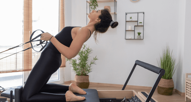 A woman exercises while bending her lower back with a reformer