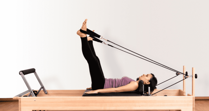 A woman doing a reformer with both legs raised