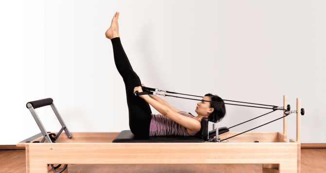 A woman who raises both legs and does a reformer