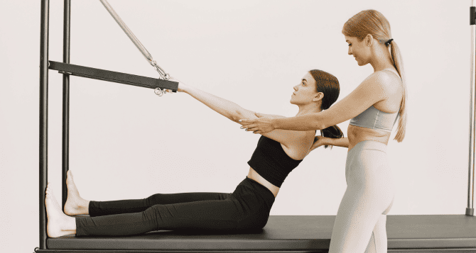 A woman and her instructor train their abdominal muscles with a reformer