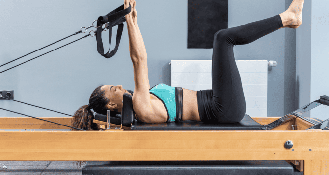 A woman using a reformer while lying on her back