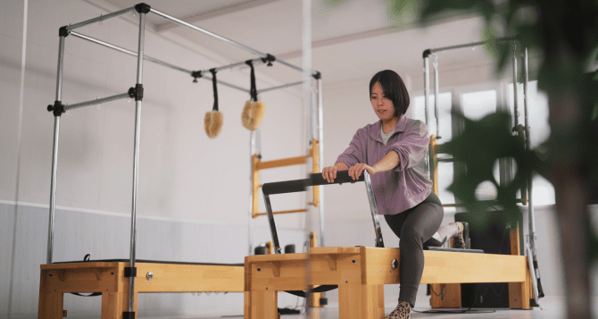 A woman wearing a purple hoodie doing a reformer