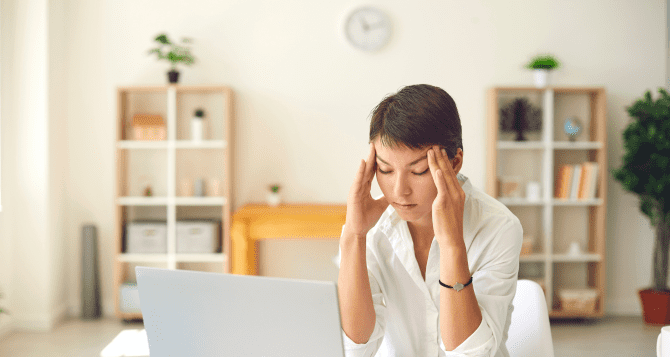 A woman holding her head in front of a computer