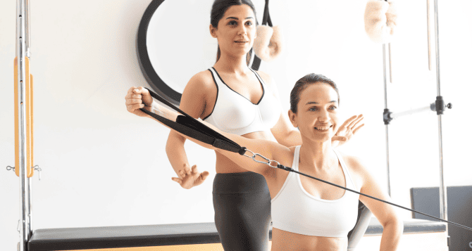 A woman using a reformer and an instructor